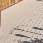a TruNorth Enviroboard Sand composite deck in warm beige tone with subtle woodgrain texture with a wooden fence and a pole
