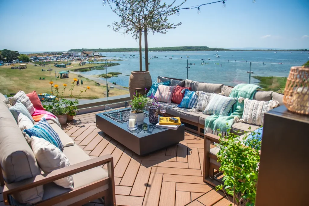 Waterfront outdoor lounge with brown composite decking, glass railings, patio seating, and coastal views, featuring Trex materials from a composite decking store in Hamilton - National Decking